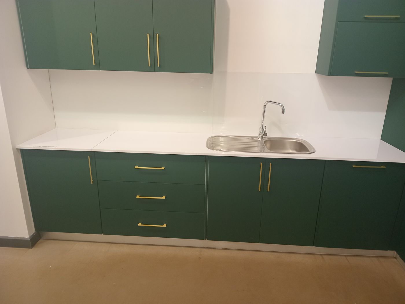 Green kitchen cabinets with brass handles and a white worktop